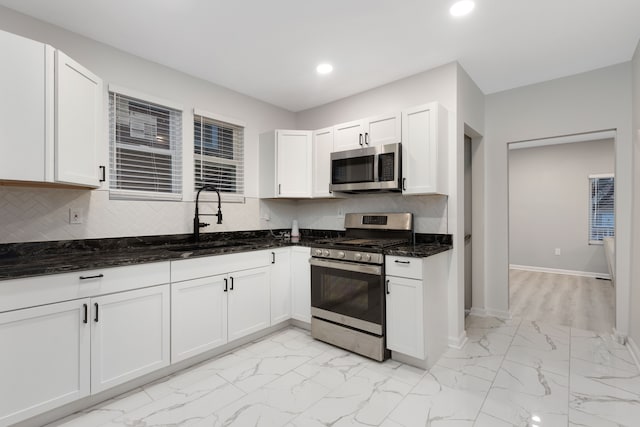 kitchen with sink, stainless steel appliances, dark stone countertops, decorative backsplash, and white cabinets