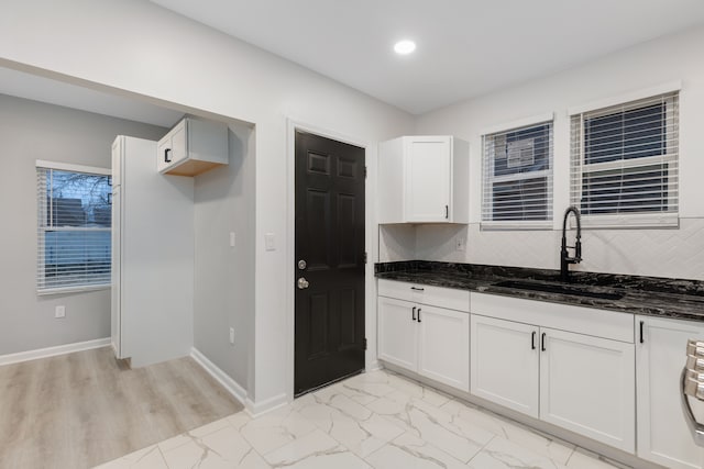 kitchen with white cabinets, sink, light hardwood / wood-style flooring, dark stone countertops, and tasteful backsplash