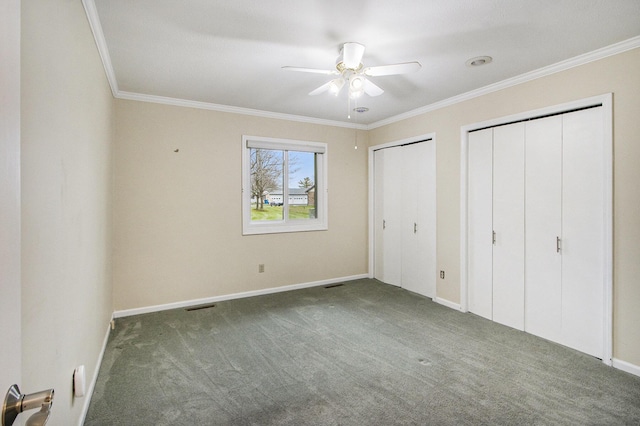 unfurnished bedroom with dark colored carpet, crown molding, ceiling fan, and multiple closets