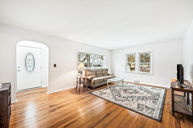 living room with arched walkways, visible vents, light wood-type flooring, and baseboards