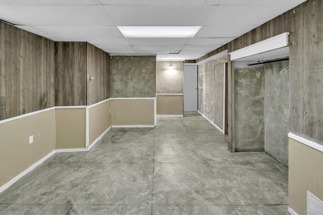 basement featuring a paneled ceiling and wood walls