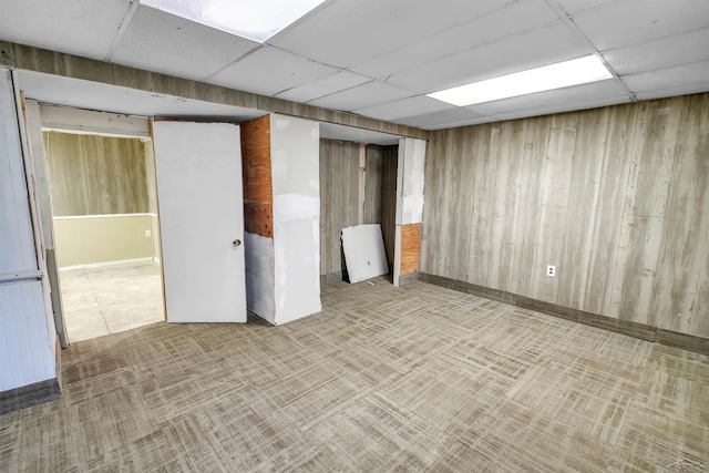 basement featuring light carpet, a paneled ceiling, and wood walls