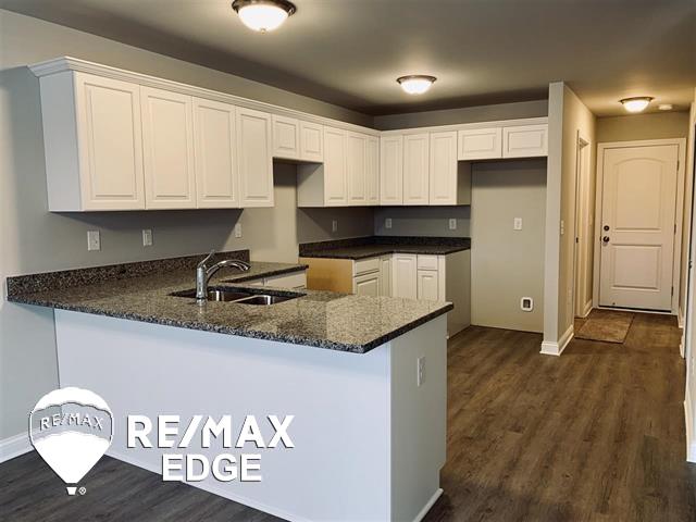 kitchen featuring white cabinetry, sink, dark hardwood / wood-style flooring, kitchen peninsula, and dark stone counters