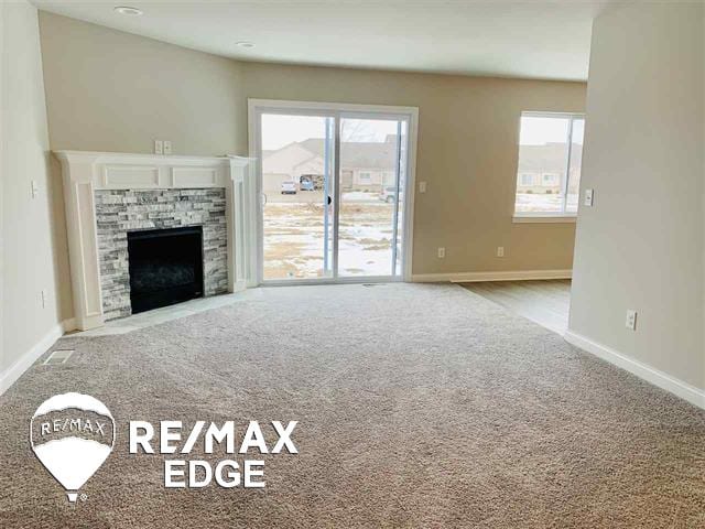 unfurnished living room featuring a stone fireplace, a wealth of natural light, and light carpet