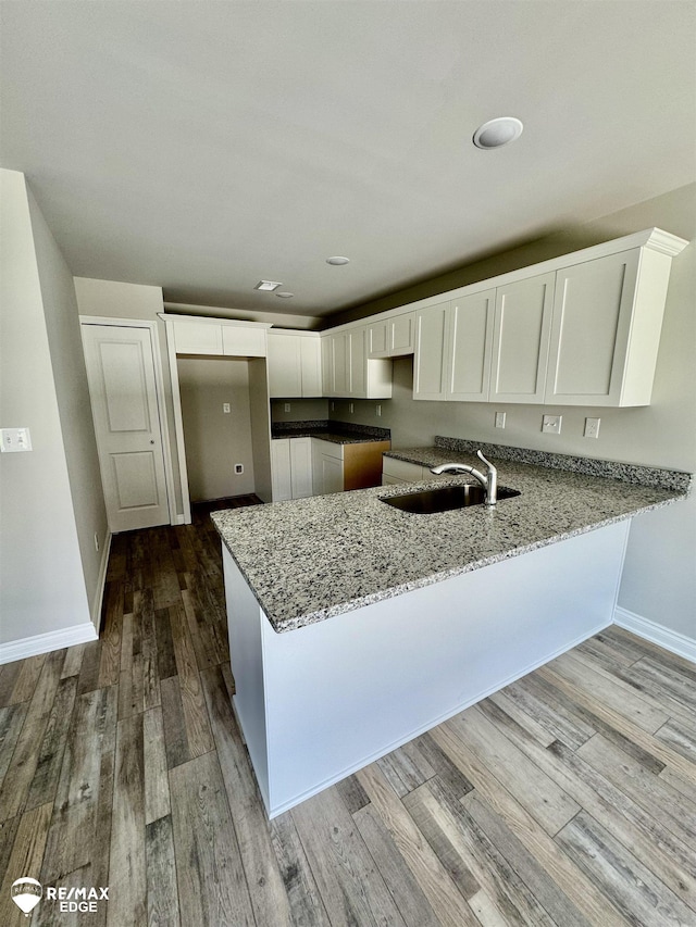 31007 Gregory St, Grand Blanc, MI 48439 - kitchen with light stone counters, a sink, a peninsula, white cabinetry, and wood finished floors