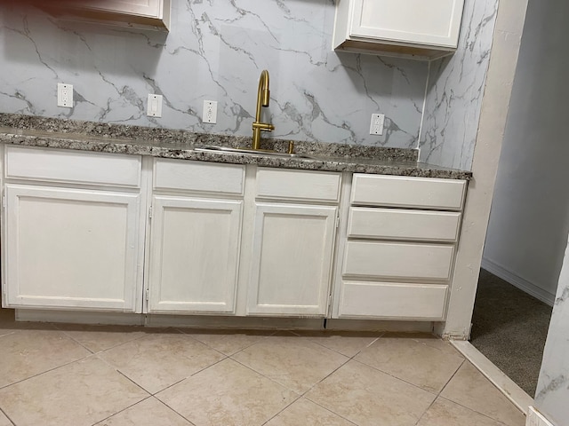 kitchen with white cabinets, light tile patterned floors, dark stone counters, and sink