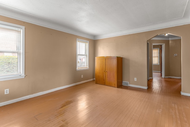 spare room featuring a textured ceiling, light hardwood / wood-style flooring, plenty of natural light, and crown molding