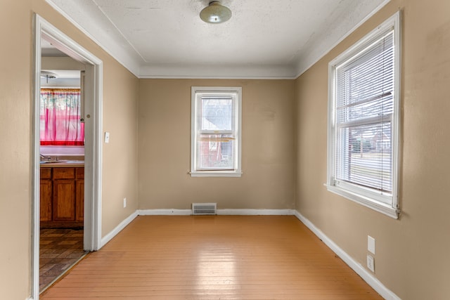 empty room with ornamental molding, a textured ceiling, and light hardwood / wood-style flooring