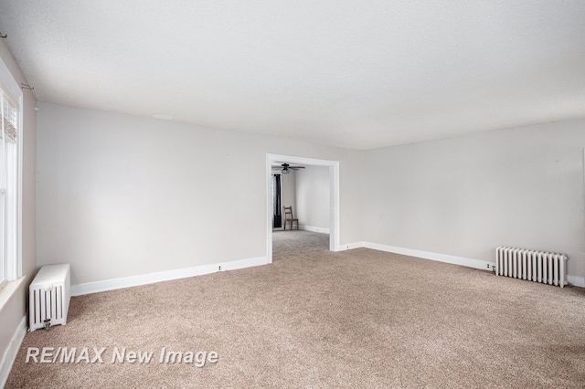 carpeted spare room featuring a healthy amount of sunlight, radiator heating unit, and a textured ceiling