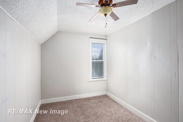 additional living space with carpet, wooden walls, vaulted ceiling, ceiling fan, and a textured ceiling