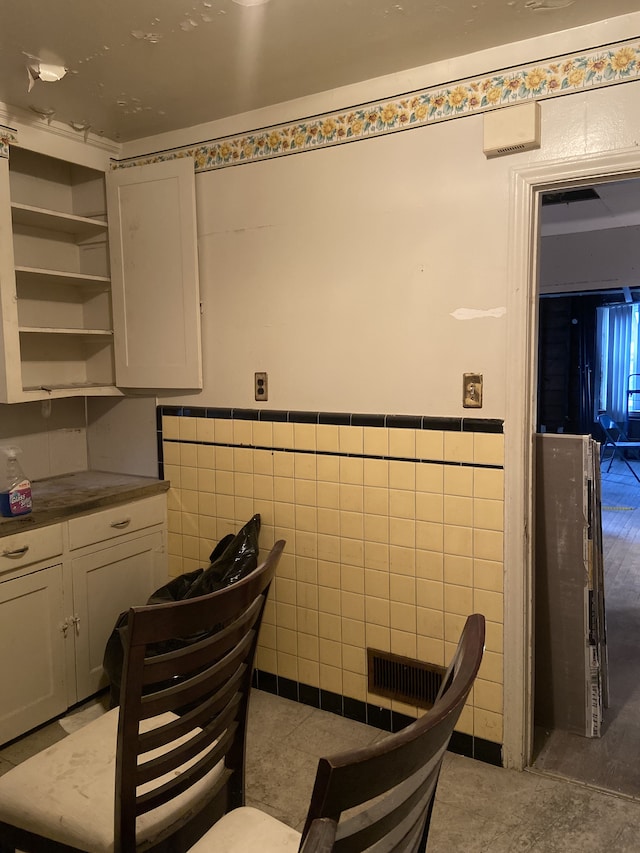 kitchen featuring dark countertops, open shelves, wainscoting, and tile walls