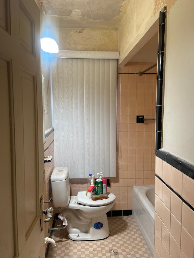 bathroom with a washtub, tile walls, and toilet