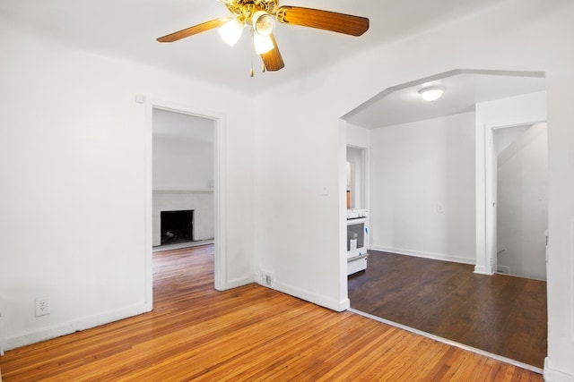 spare room with hardwood / wood-style flooring, a brick fireplace, and ceiling fan