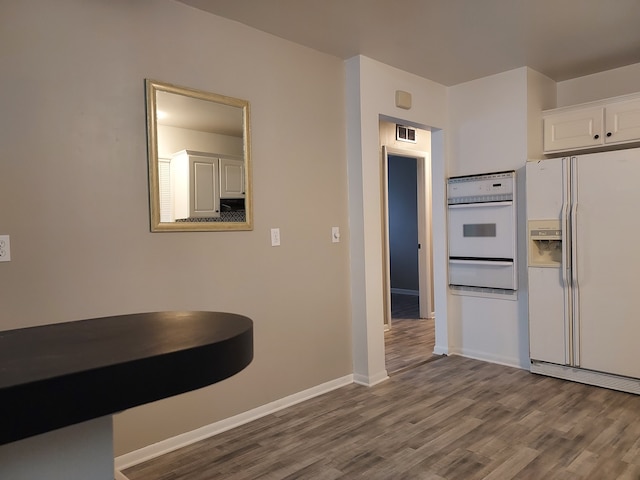 kitchen with wood-type flooring, white appliances, and white cabinetry