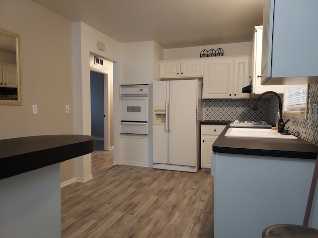 kitchen with decorative backsplash, white appliances, sink, light hardwood / wood-style flooring, and white cabinets