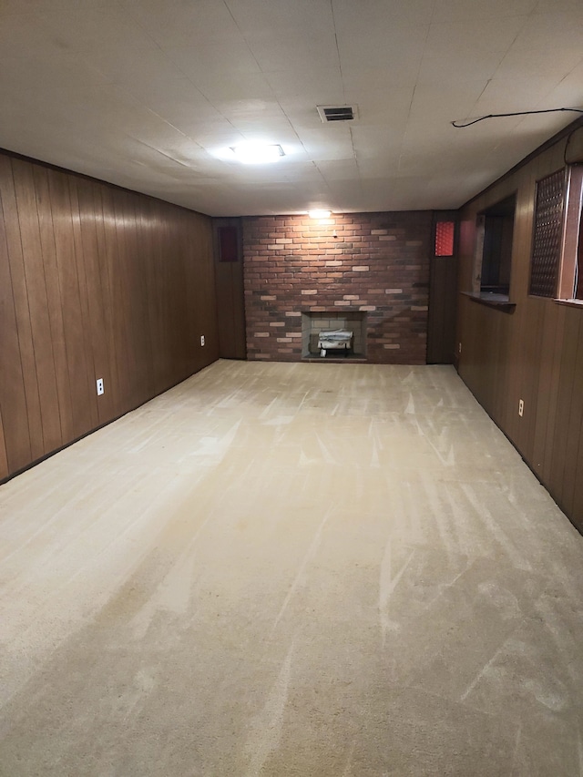 basement with wood walls, light colored carpet, and a brick fireplace