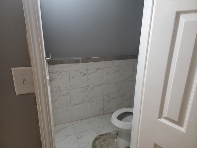 bathroom featuring marble finish floor, toilet, and tile walls