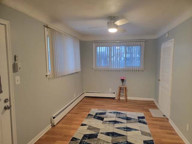 interior space with baseboard heating, baseboards, light wood-style floors, and a ceiling fan