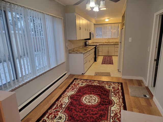 kitchen featuring tasteful backsplash, freestanding refrigerator, baseboard heating, ceiling fan, and stainless steel gas range