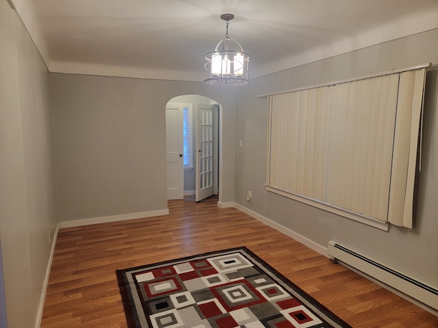 empty room with wood finished floors, baseboards, arched walkways, a baseboard heating unit, and a notable chandelier