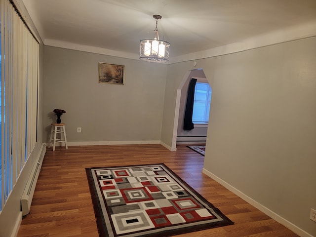 interior space featuring wood finished floors, arched walkways, an inviting chandelier, a baseboard radiator, and baseboards