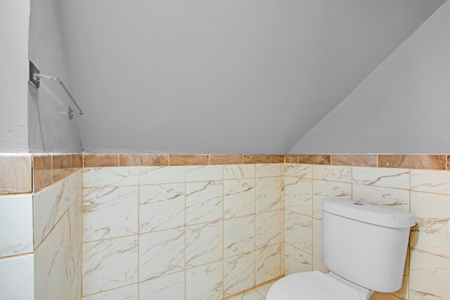 bathroom with vaulted ceiling, toilet, tile walls, and a shower