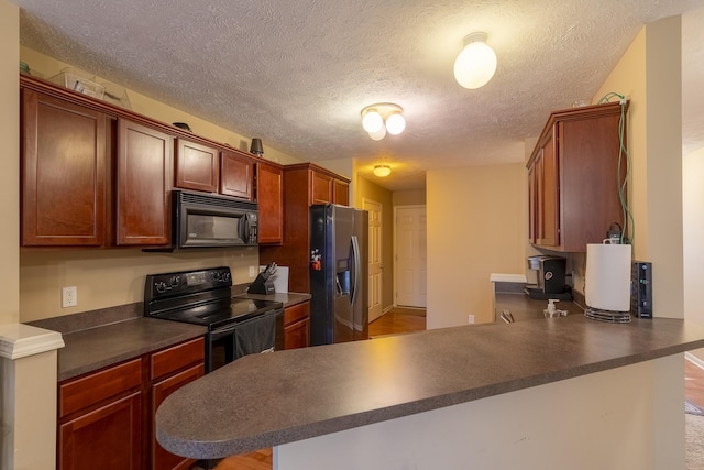 kitchen featuring kitchen peninsula, a breakfast bar, black appliances, and a textured ceiling