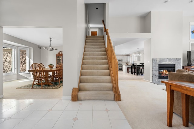 stairway featuring a high end fireplace, carpet, and a notable chandelier