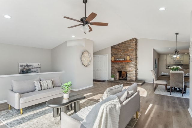 living room with ceiling fan with notable chandelier, a stone fireplace, lofted ceiling, and dark wood-type flooring