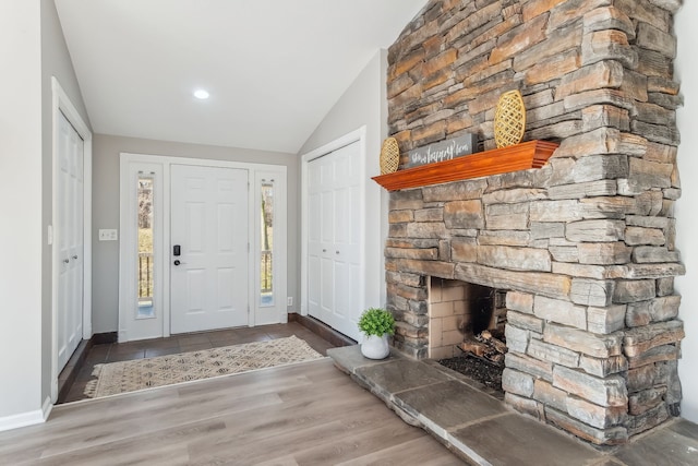 foyer featuring a stone fireplace, lofted ceiling, and dark wood-type flooring