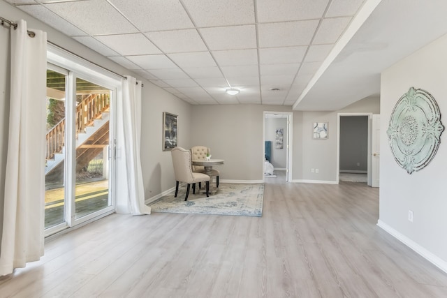 living area with a drop ceiling and light wood-type flooring