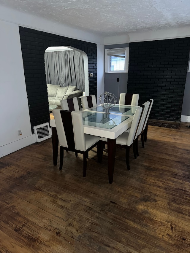 dining space featuring a textured ceiling, dark wood-type flooring, and brick wall