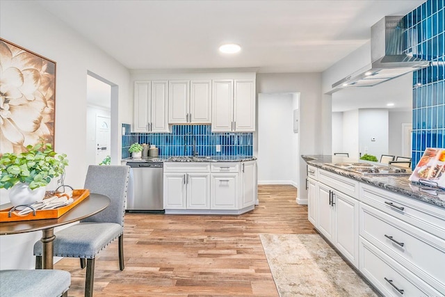 kitchen featuring dark stone counters, wall chimney exhaust hood, stainless steel appliances, light hardwood / wood-style flooring, and white cabinetry