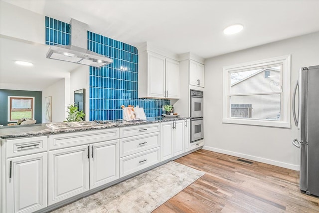 kitchen with stone counters, light hardwood / wood-style flooring, backsplash, white cabinets, and appliances with stainless steel finishes