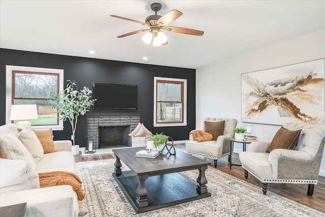 living room with ceiling fan, wood-type flooring, and a brick fireplace