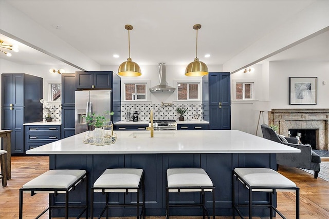 kitchen featuring decorative backsplash, a breakfast bar, wall chimney range hood, stainless steel fridge with ice dispenser, and hanging light fixtures