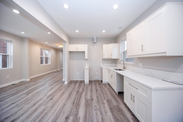 kitchen featuring light stone countertops, sink, white cabinets, and light hardwood / wood-style floors