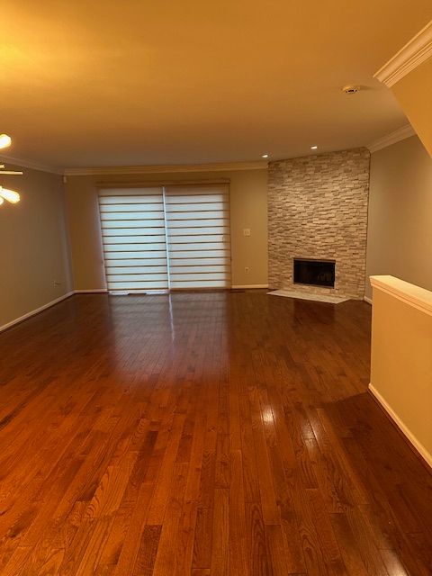 unfurnished living room featuring a stone fireplace, hardwood / wood-style floors, and ornamental molding