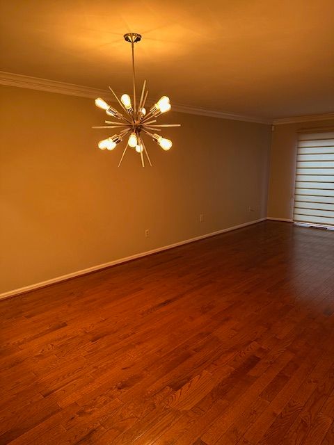 unfurnished room with a chandelier, ornamental molding, and dark wood-type flooring