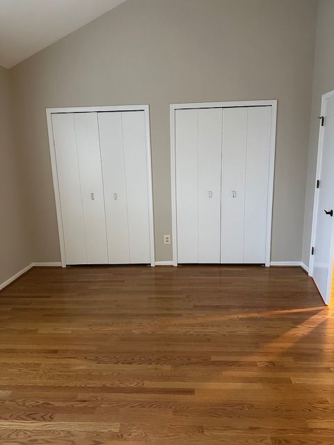 unfurnished bedroom with dark hardwood / wood-style flooring, high vaulted ceiling, and multiple closets