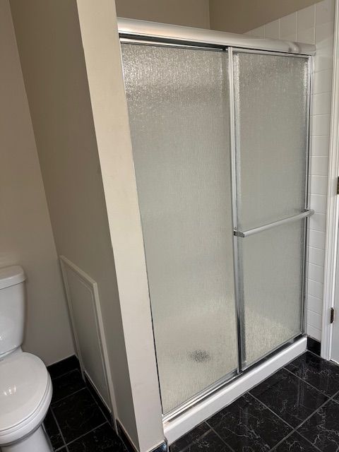 bathroom featuring tile patterned floors, toilet, and a shower with door