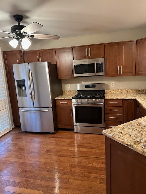 kitchen with ceiling fan, dark hardwood / wood-style flooring, light stone countertops, and appliances with stainless steel finishes