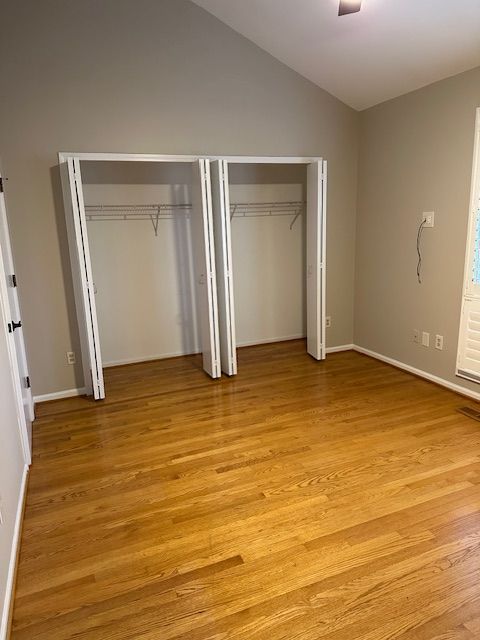 unfurnished bedroom featuring two closets, lofted ceiling, and light wood-type flooring