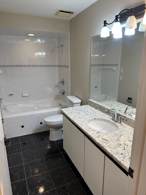 full bathroom featuring tile patterned floors, vanity, tiled shower / bath combo, and toilet