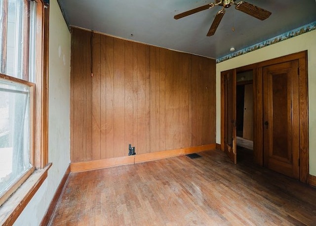 unfurnished room featuring wooden walls, ceiling fan, and hardwood / wood-style flooring