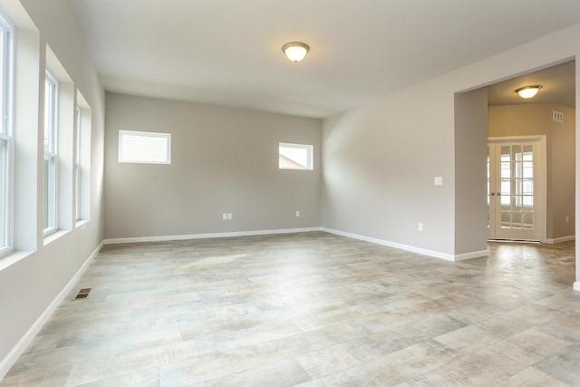 spare room with light wood-type flooring, visible vents, and baseboards