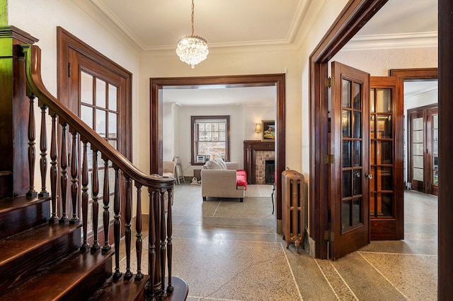 foyer entrance featuring radiator, french doors, a brick fireplace, a notable chandelier, and crown molding