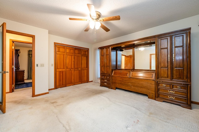 unfurnished bedroom featuring ceiling fan, light colored carpet, a textured ceiling, and a closet