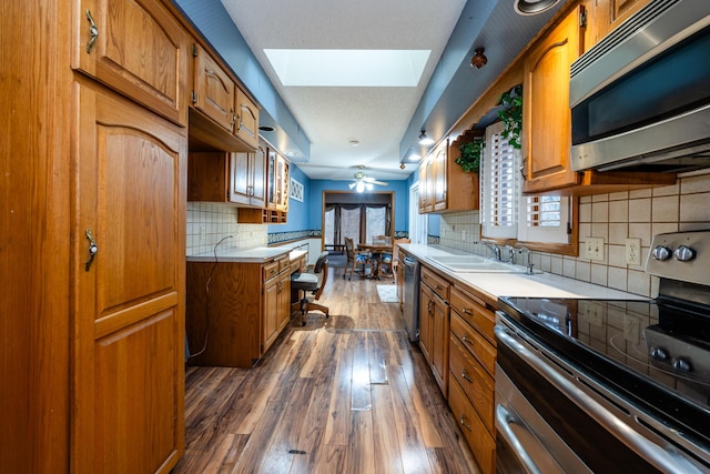 kitchen featuring backsplash, a skylight, dark hardwood / wood-style floors, ceiling fan, and stainless steel appliances