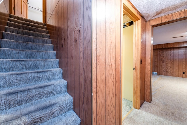 stairs featuring carpet floors, a textured ceiling, and wooden walls